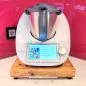 Preview: Gleitbrett / Rollbrett aus Massivholz für Thermomix, Farbe honey, mit eckigem Edelstahlgriff, in Küche mit Glas-Rückwand